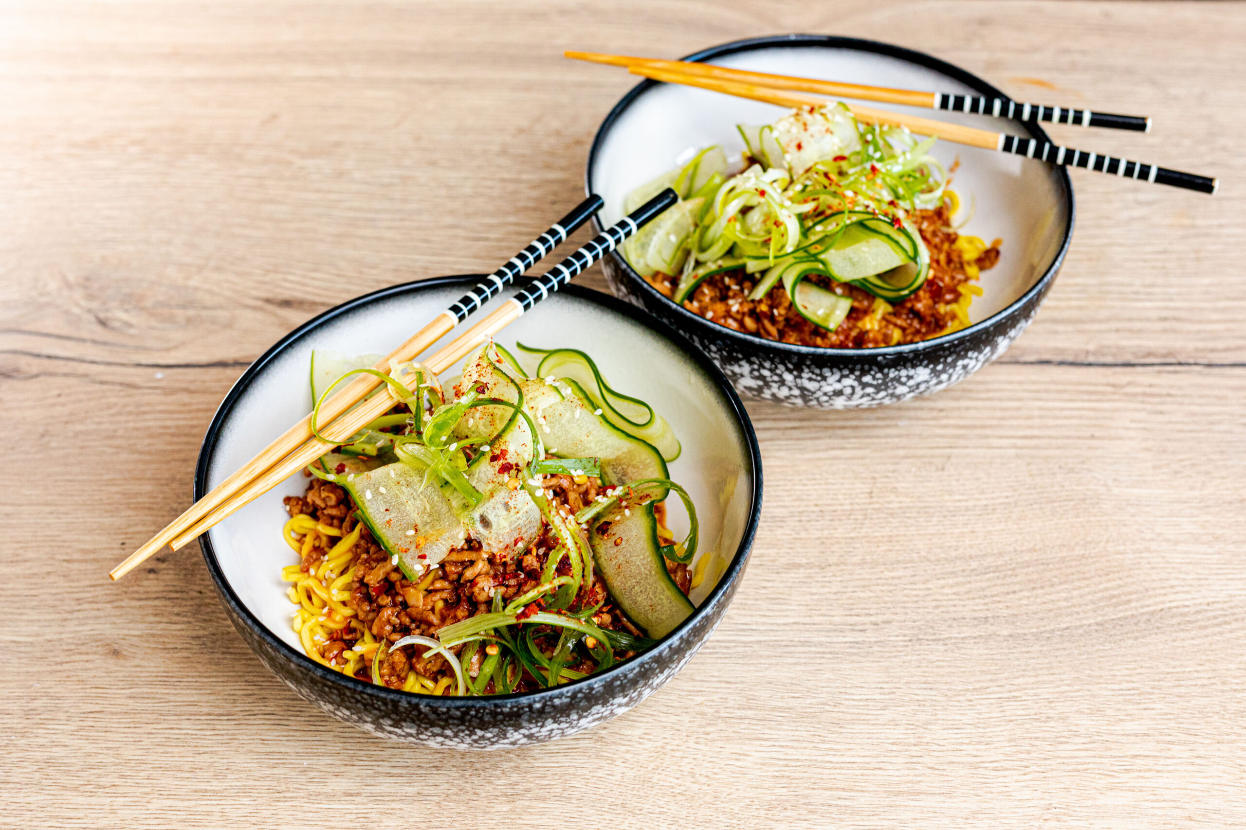 Two bowls of dan dan noodles with cucumber