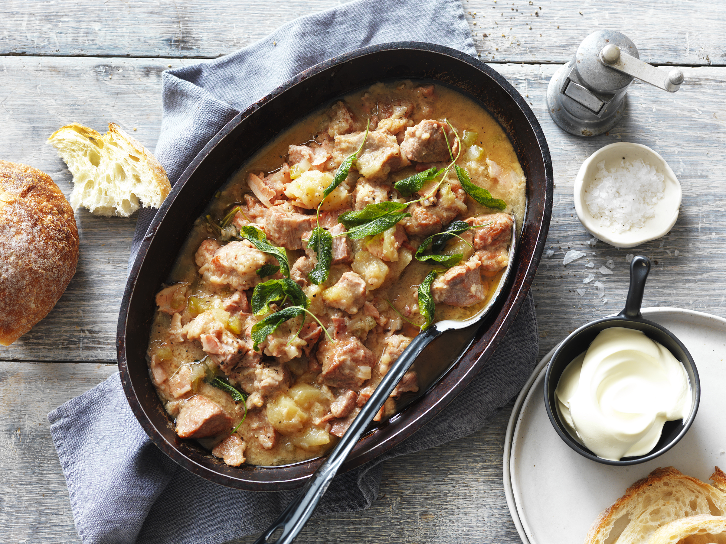 Pork and apple cider casserole in an oval dish on a table scape surrounded by condiments